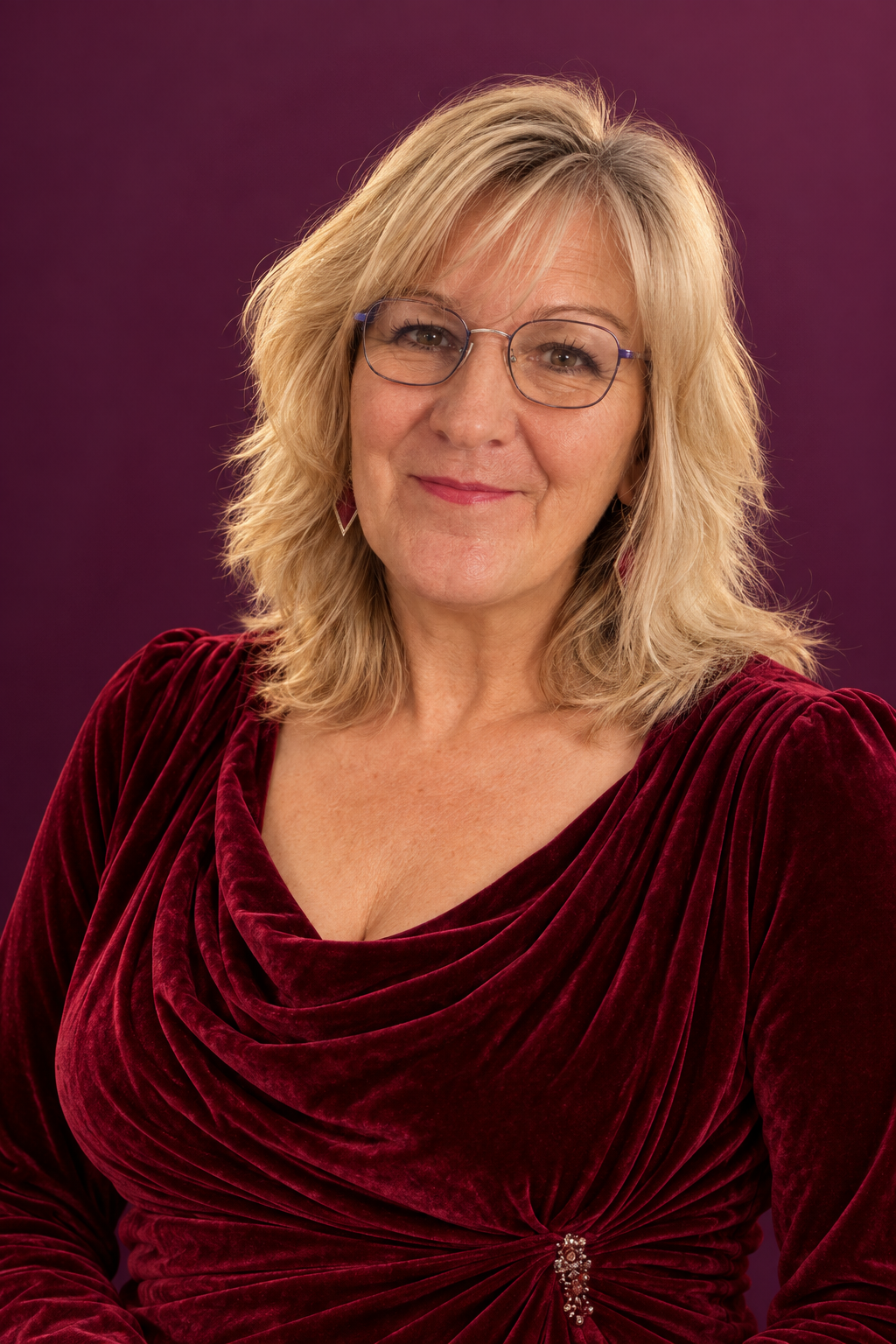 Cleo Van Saar mit blonden Haaren, runder Brille und weinrotem Samtoberteil